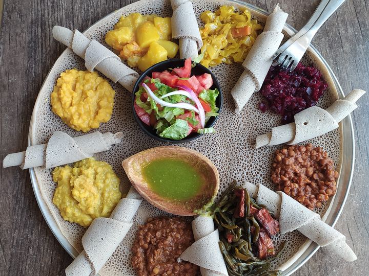 A large round injera topped with eight different Ethiopian stews and vegetables
