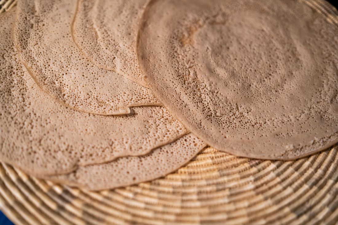 Folded rounds of pale injera made from ivory teff in a woven basket