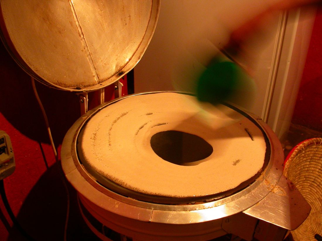 A cook pouring injera batter in a spiral onto a large hot griddle