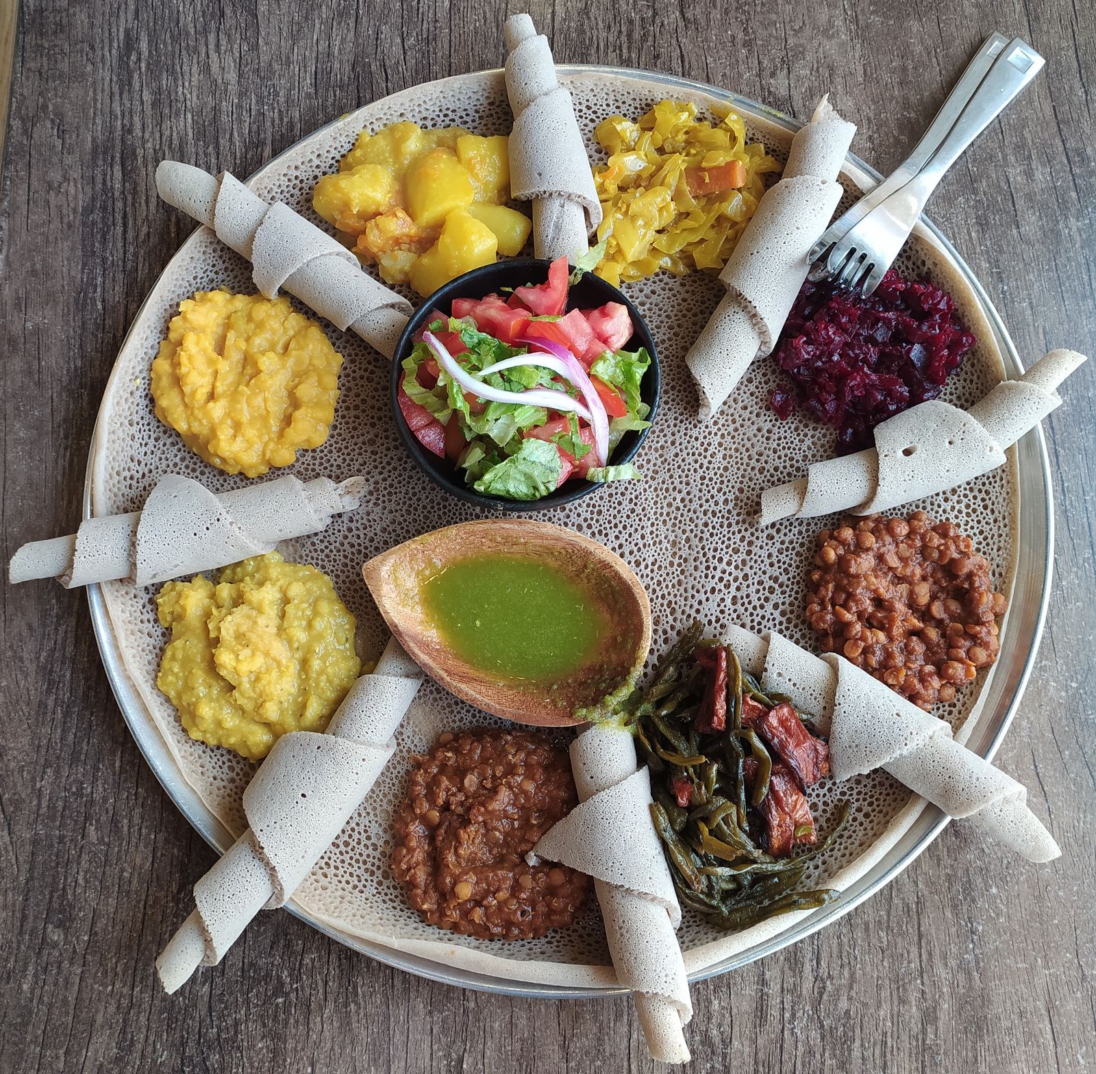 A large round injera topped with eight different Ethiopian stews and vegetables