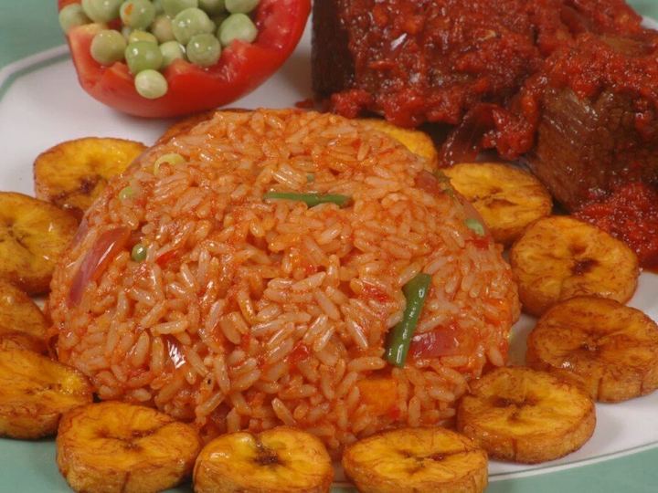 A plate of red-orange jollof rice served with fried plantain slices