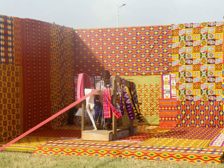 Kente weavers at work on narrow-strip looms in Ghana, with long warp threads stretched out in front