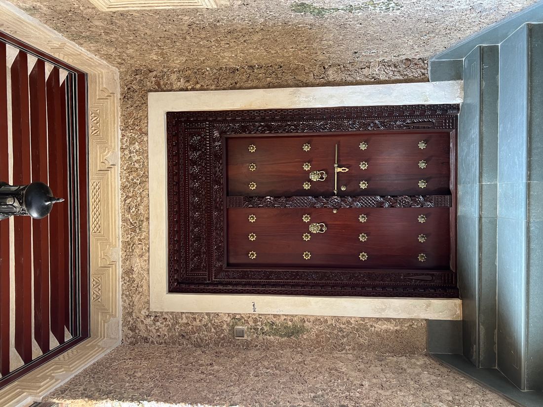 A heavy carved wooden door set in a coral stone wall in Lamu Old Town