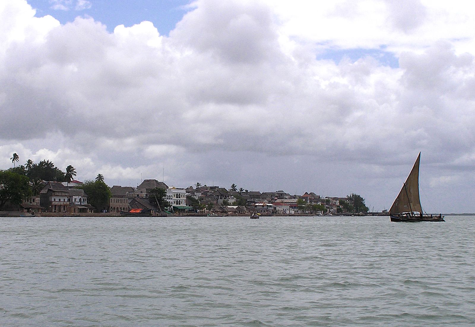 The seafront of Lamu Town in Kenya seen from the water, with a dhow under sail
